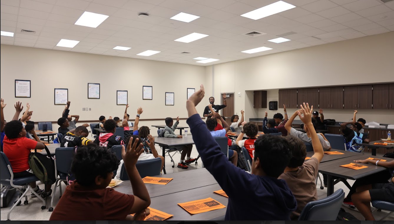 Coach leading an engaged workshop of middle and high school students with hands raised